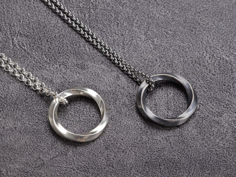 May include: Two silver-toned pendant necklaces. Each necklace features a circular pendant with a twisted design, suspended from a delicate chain. The pendants have a polished finish, and the chains are also silver.