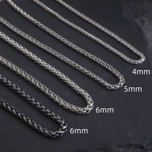 May include: Several silver wheat chain necklaces of different thicknesses. The image shows sizes 4mm, 5mm, and 6mm, displayed on a dark background. One necklace is a darker, gunmetal colour.
