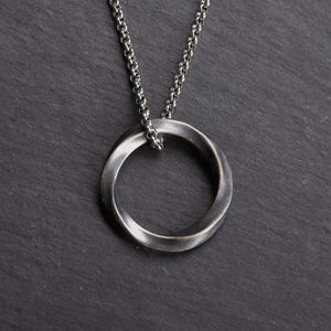 May include: A silver-toned pendant necklace featuring a twisted Mobius strip design. The pendant hangs from a delicate chain. The jewelry is displayed against a dark, textured background.