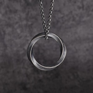 May include: A silver-toned pendant necklace featuring a Mobius strip design. The pendant is a continuous loop, suspended from a matching chain. The necklace is displayed against a dark gray background, highlighting the metallic finish.