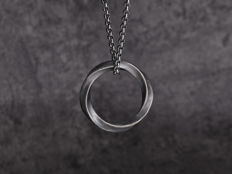 May include: A silver-toned pendant necklace featuring a Mobius strip design. The pendant is a continuous loop, suspended from a matching chain. The necklace is displayed against a dark gray background, highlighting the metallic finish.