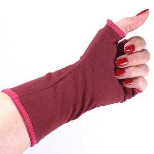 Könnte beinhalten: Ein fingerloser Handschuh in Rotbraun mit rosa Besatz. Der Handschuh wird an einer Hand mit rotem Nagellack getragen.