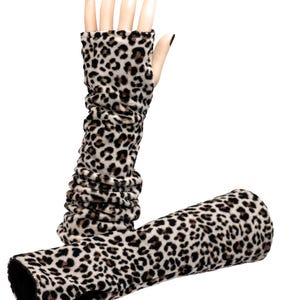 May include: A pair of long, leopard print arm warmers. The arm warmers are made of a soft, plush material with a black and brown spotted pattern on a cream background. The arm warmers are displayed on a mannequin hand.