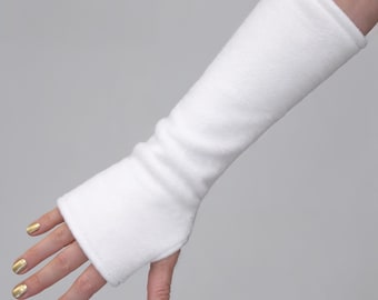 Op de afbeelding: Een lange, vingerloze handschoen in wit, gemaakt van een zachte, fleece-achtige stof. De handschoen reikt van de knokkels tot aan de onderarm en heeft een eenvoudig, recht ontwerp met een opening voor de duim en een brede opening voor de vingers.