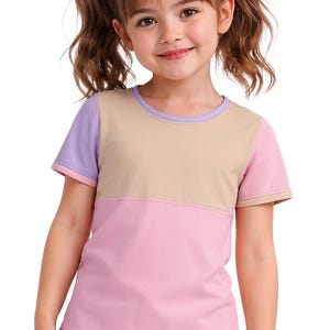 Könnte beinhalten: Ein farbblock-T-Shirt in Pastelltönen aus Rosa, Beige und Lila. Das kurzärmelige Oberteil hat einen runden Ausschnitt und wird von einem jungen Mädchen getragen. Das Mädchen trägt ihr Haar in Zöpfen mit rosa Haargummis.