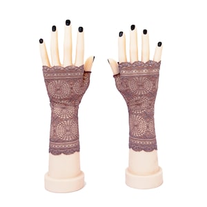 Peut inclure: Une paire de gants sans doigts en dentelle marron avec un motif circulaire. Les gants s'étendent des articulations jusqu'au milieu de l'avant-bras et présentent un bord festonné en haut et en bas, présentés sur deux mains de mannequin pâles.
