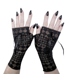 May include: A pair of black fingerless gloves featuring a detailed diamond pattern throughout the fabric. Each glove is accented with a small black ribbon bow at the wrist area and finished with a delicate scalloped edge along the top opening.