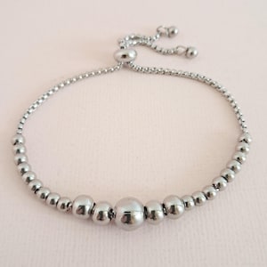 May include: A silver beaded bracelet with a sliding clasp. The bracelet has a row of larger beads in the centre.