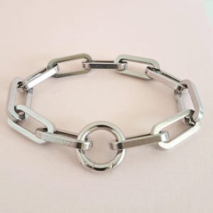 May include: A silver chain bracelet with a large, round clasp. The bracelet is made of interlocking oval links.