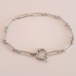 May include: A silver chain bracelet with a toggle clasp. The chain is made of rectangular links.