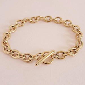 May include: A gold chain bracelet with a toggle clasp. The chain is made of thick, oval-shaped links.