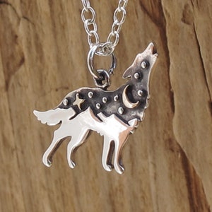 sterling silver wolf pendant an oxidized top half of the wolf has a raised bronze star and moon adding texture the bottom half of the wolf has a polished mountain landscape the wolf has head raised as if howling