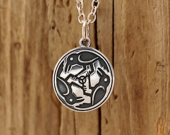 Könnte beinhalten: Silberne Halskette mit Anhänger, der ein kreisförmiges Design mit drei stilisierten Vögeln in einem Kreis zeigt. Die Vögel sind schwarz und der Hintergrund ist silber.