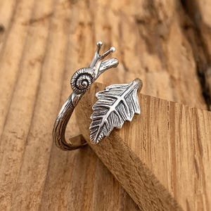 May include: Silver ring featuring a snail on a twig design with a leaf detail.