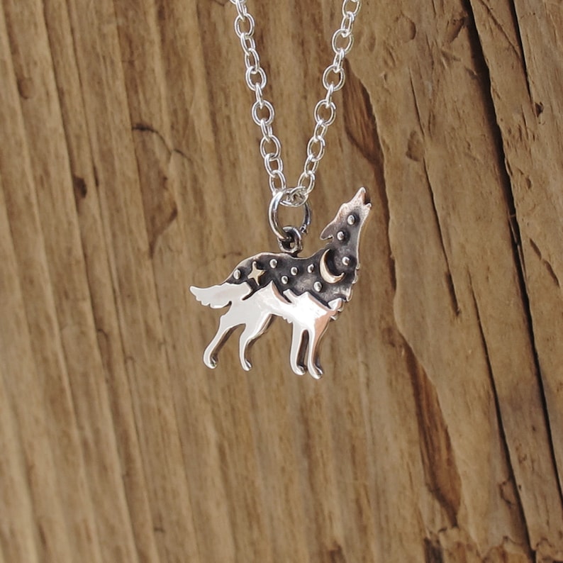 sterling silver wolf pendant an oxidized top half of the wolf has a raised bronze star and moon adding texture the bottom half of the wolf has a polished mountain landscape the wolf has head raised as if howling