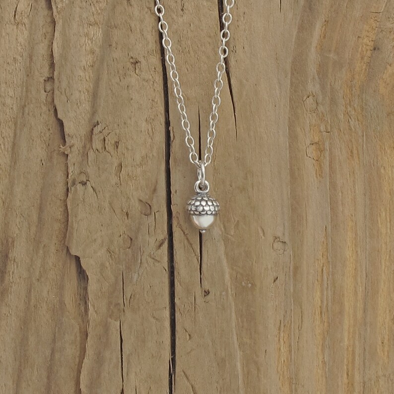 May include: A silver acorn pendant necklace on a silver chain. The pendant is small and detailed, with a textured surface.