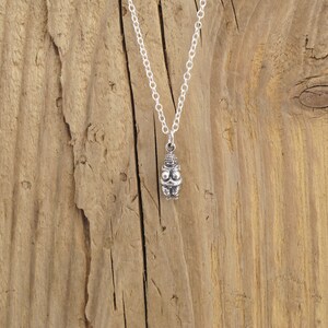 May include: Silver necklace with a small, detailed pendant depicting a female figure. The pendant is on a silver chain against a wooden background.