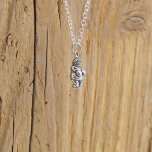 May include: A silver necklace with a small, detailed pendant of a person in a seated pose.