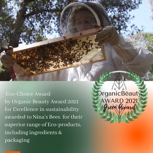 Eco Choice award for Organic Beauty Award 2021 for excellence in sustainability awarded to Ninas bEES FOR THEIR SUPERIOR RANGE OF ECO PRODUCTS, INCLUDING INGREDIENTS AND PACKAGING. THE PHOTO DEPICTS NINA IN BEEKEEPING SUIT HOLDING A FRAME  HONEYCOMB