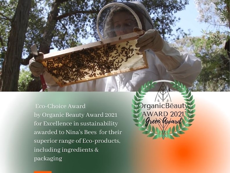 Eco Choice award for Organic Beauty Award 2021 for excellence in sustainability awarded to Ninas bEES FOR THEIR SUPERIOR RANGE OF ECO PRODUCTS, INCLUDING INGREDIENTS AND PACKAGING. THE PHOTO DEPICTS NINA IN BEEKEEPING SUIT HOLDING A FRAME  HONEYCOMB