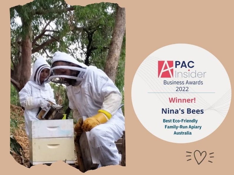 Ninas Bees received an award for being best eco friendly family run apiary. the picture shows an adult beekeeper kneeling next to the hive. A little child in a beekeeper suit is assisting the beekeeper with the smoker