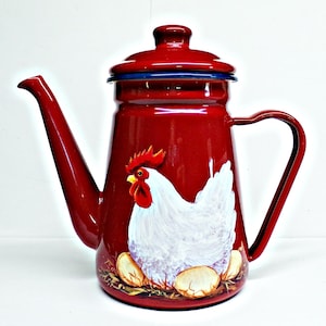May include: A red enamelware coffee pot with a white chicken and egg design. The pot has a long spout, a handle, and a lid with a blue rim. The chicken is painted on the front of the pot, with eggs at the bottom.