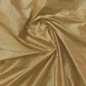 Puede incluir: Primer plano de una tela suave y dorada con un brillo sutil. La tela est&aacute; drapeada y doblada, creando l&iacute;neas suaves y fluidas.