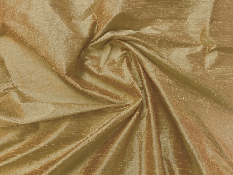 Puede incluir: Primer plano de una tela suave y dorada con un brillo sutil. La tela est&aacute; drapeada y doblada, creando l&iacute;neas suaves y fluidas.