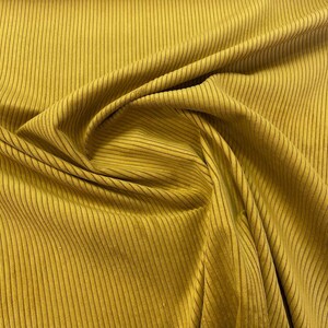 K&ouml;nnte beinhalten: Senfgelber Rippstoff mit vertikalen Linien. Der Stoff ist drapiert und erzeugt Falten und Schatten, die die Textur hervorheben. Die Farbe ist ein warmer, erdiger Ton, der sich f&uuml;r Kleidung oder Heimdekoration eignet.