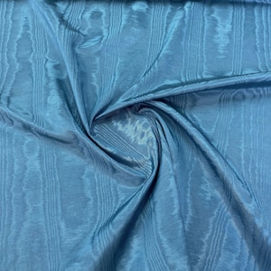 Könnte beinhalten: Nahaufnahme eines blauen Stoffes mit einem strukturierten, gewebten Muster. Der Stoff ist gefaltet und drapiert und zeigt seine weiche und fließende Textur.