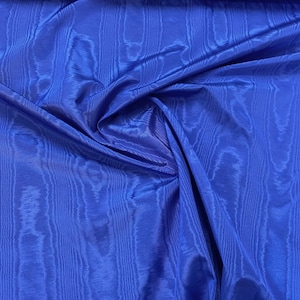 Könnte beinhalten: Eine Nahaufnahme eines leuchtend blauen Stoffes mit einem strukturierten, gewebten Muster. Der Stoff ist weich und fällt wunderschön, was seine luxuriöse Haptik unterstreicht.