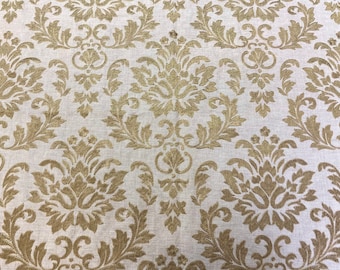 May include: Close-up of a fabric with a repeating damask pattern. The design features ornate, stylized floral and leaf motifs in a gold color against a light beige background. The fabric has a textured appearance.