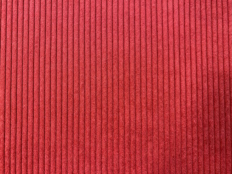 K&ouml;nnte beinhalten: Nahaufnahme eines Cordstoffes in einem warmen, r&ouml;tlich-orangen Farbton. Die vertikalen Rippen erzeugen ein geripptes Muster, das dem Textil Tiefe und visuelles Interesse verleiht. Geeignet f&uuml;r verschiedene N&auml;h- und Bastelprojekte.