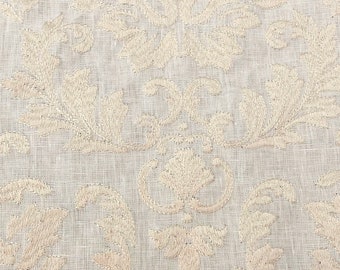 May include: A close-up of a white fabric with an embroidered floral pattern. The fabric has a subtle texture and a delicate, intricate design.