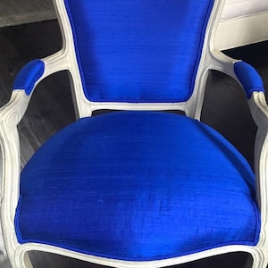 Puede incluir: Un sill&oacute;n de madera blanca con un asiento y respaldo de terciopelo azul. El sill&oacute;n tiene un respaldo y brazos curvos, y las patas est&aacute;n talladas en un estilo tradicional.