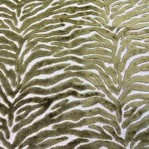 May include: Close-up of a fabric with a zebra stripe pattern. The design features olive green stripes against a white background. The fabric has a textured, plush appearance, suggesting a soft material.
