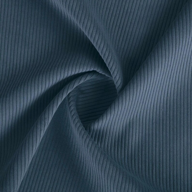 K&ouml;nnte beinhalten: Nahaufnahme eines gefalteten St&uuml;cks blauen Cordstoffs. Der Stoff hat eine gerippte Textur mit vertikalen Linien, die das Material hinunterlaufen. Die Farbe ist ein ged&auml;mpftes, staubiges Blau, und der Stoff wirkt weich und geschmeidig.