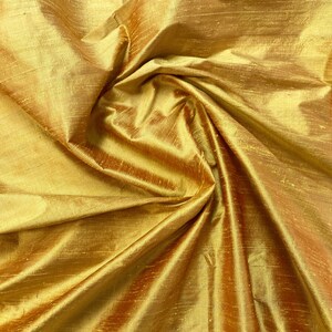 Puede incluir: Primer plano de una tela de seda dorada con un brillo sutil. La tela est&aacute; drapeada y doblada, creando una textura suave y lujosa.