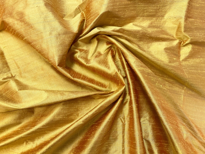 Puede incluir: Primer plano de una tela de seda dorada con un brillo sutil. La tela est&aacute; drapeada y doblada, creando una textura suave y lujosa.