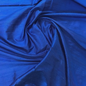 Puede incluir: Primer plano de una tela lisa de color azul real con un brillo sedoso. La tela est&aacute; drapeada y doblada, creando l&iacute;neas suaves y fluidas.