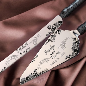 Op de afbeelding: Een taartmes en serveerset met zwarte handvatten en zilveren bladen. De bladen zijn versierd met bloemen- en skelet handontwerpen, en bevatten de tekst "Till death do us part" en namen met een datum.