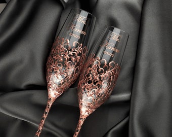May include: Two champagne flutes with rose gold detailing and a decorative floral pattern. The flutes are personalized with the text "Mr. & Mrs. (Last Name)".