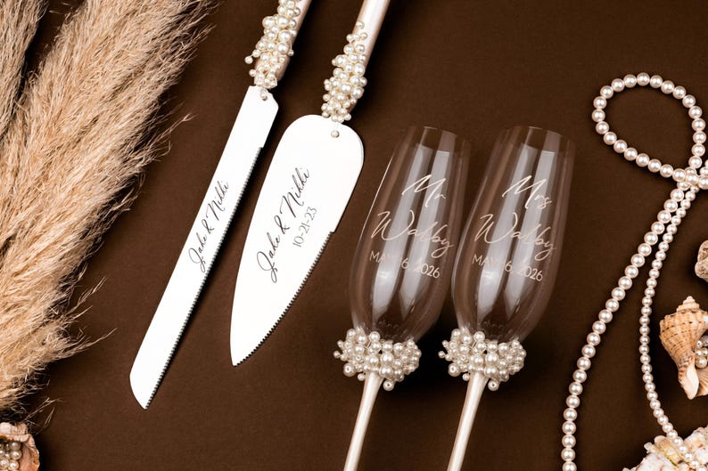 Puede incluir: Juego de cuchillo y servidor de pastel de bodas con detalles de perlas, personalizado con nombres y fecha. Dos copas de champ&aacute;n con bases de perlas y el texto "Mr & Mrs Walby" y la fecha 6 de mayo de 2026. Perlas decorativas y conchas marinas.