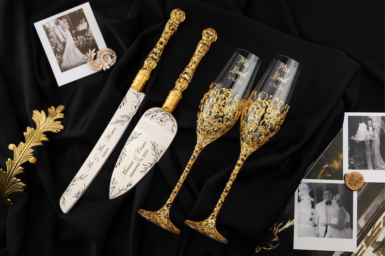 May include: Gold wedding cake knife and server set with a floral design and the text "Mr. & Mrs. (names) September 18, 2023". Two gold-rimmed champagne flutes with the text "Mr. Bond 5/6/23" and "Mrs. Bond 5/6/23".