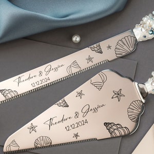 Peut inclure: Ensemble de couteau et de pelle à gâteau argentés, gravés de coquillages et d'étoiles de mer. Les manches sont ornés de perles blanches, bleues et couleur perle. Les noms "Theodore & Jessica" et la date "12.12.2024" sont gravés.