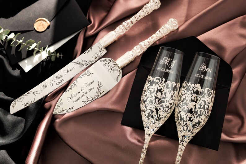 May include: A wedding cake cutting set with two silver knives and two champagne flutes. The knives are engraved with the names "Mr. & Mrs. Homes" and "Miriam & Cesar" with their wedding date. The champagne flutes are engraved with the names "MJ" and "Ben" with their wedding dates.