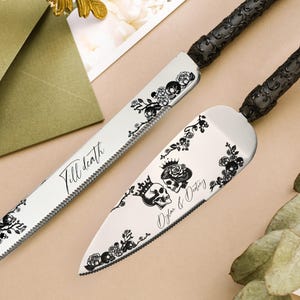 May include: A silver cake knife and server set with black ornate handles. The blades feature black etched floral patterns, skull illustrations, and the text "Till death" on the knife and "Dylan & Destiny" on the server blade.