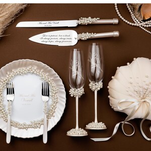 Puede incluir: Conjunto de boda elegante con cuchillo y servidor de pastel, dos copas de champ&aacute;n, una almohada para anillos y un plato decorativo, todos adornados con perlas. El conjunto incluye los nombres de la pareja y la fecha de la boda.