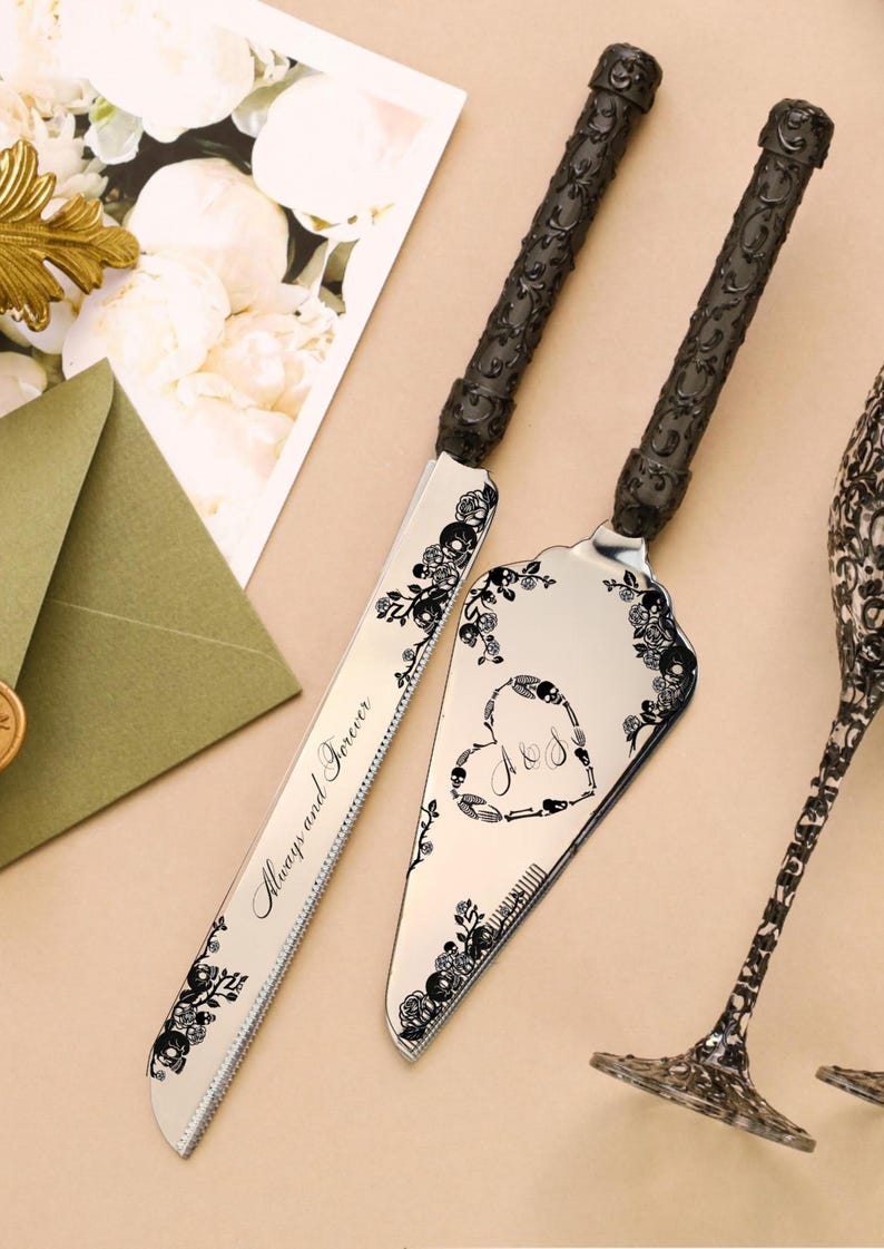 May include: Silver cake knife and server set with black floral and skull accents. The knife is engraved with "Always and Forever". The server features a heart design with initials. The handles are black.