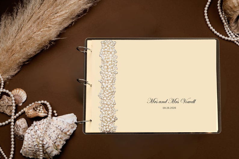 Puede incluir: Un libro de visitas de boda color crema con una columna vertebral con cuentas de perlas. El libro est&aacute; abierto, mostrando el texto "Mrs and Mrs Vowell" y la fecha "09.26.2026". Conchas marinas y perlas decorativas rodean el libro.